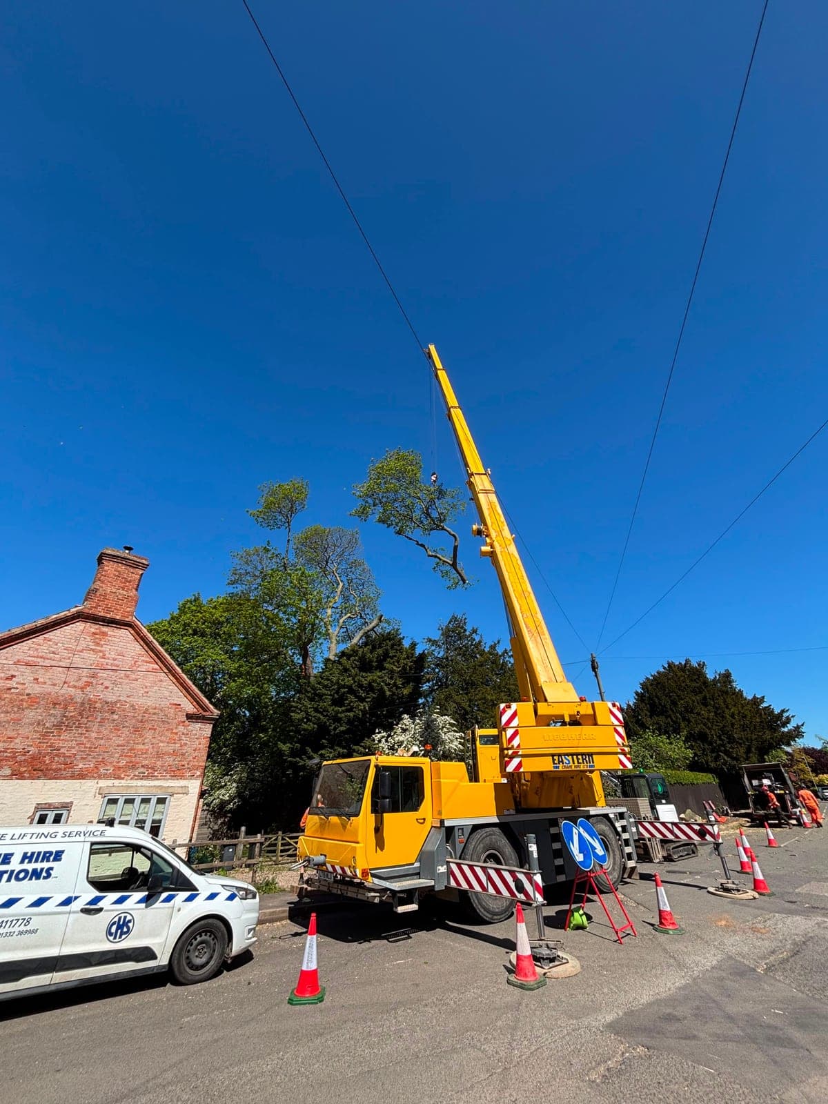 Mobile crane removing a tree beside a country cottage