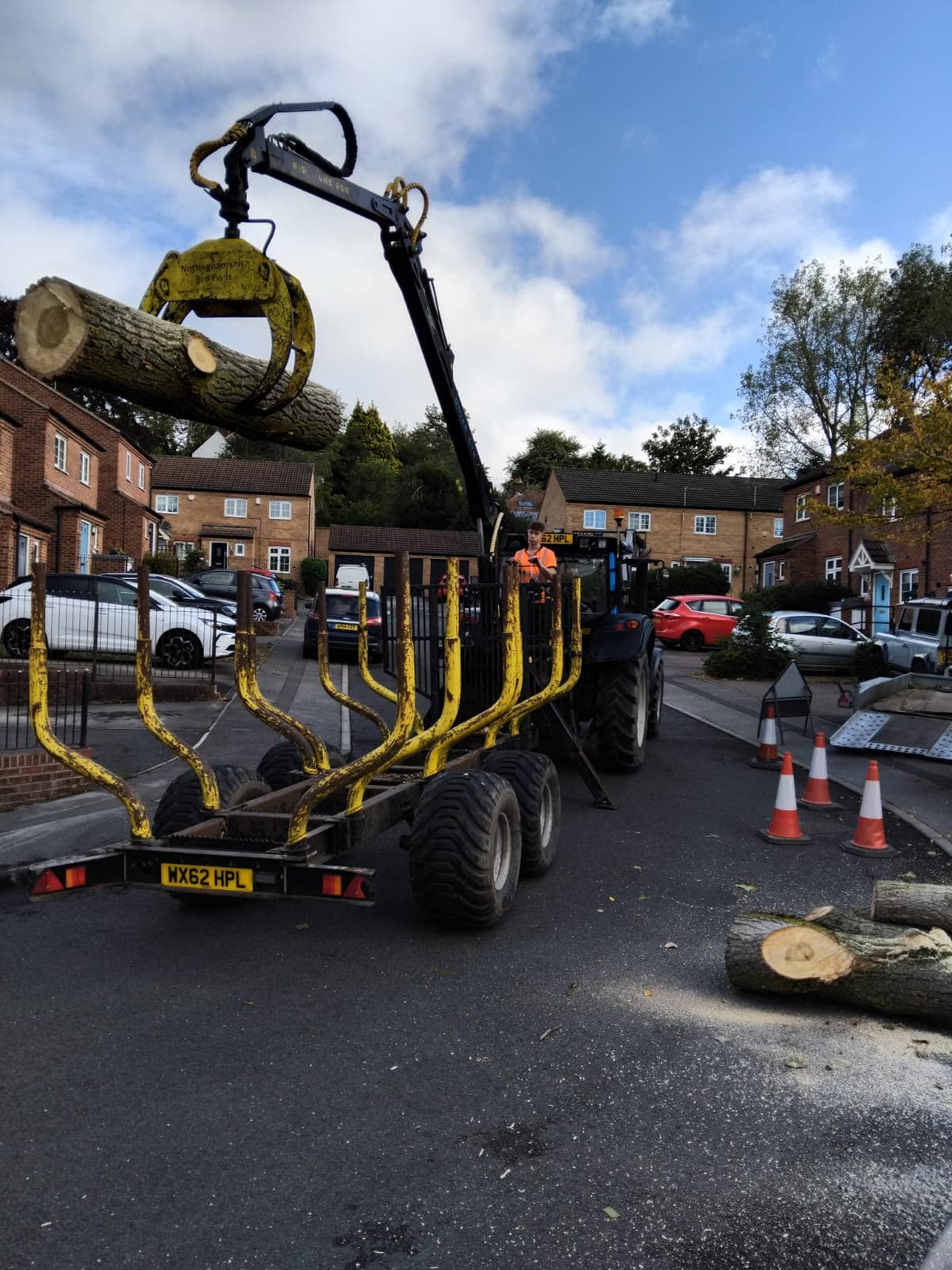 Tractor-mounted timber crane lifting a log on a residential street